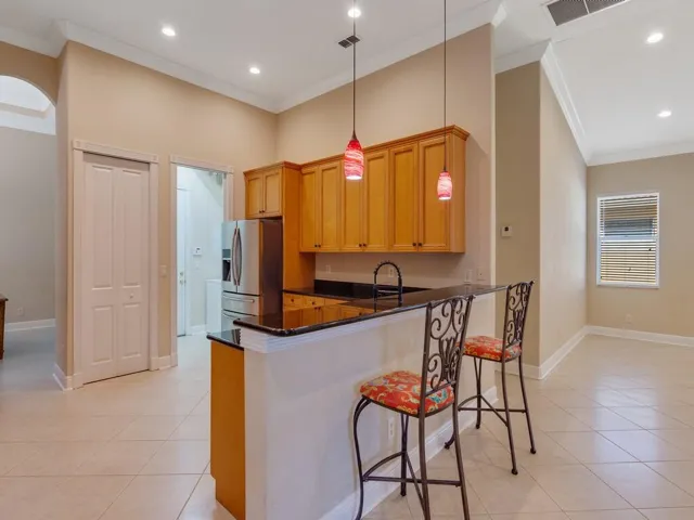 Kitchen with crown molding, a kitchen breakfast bar, decorative light fixtures, light tile patterned flooring, and dark stone countertops