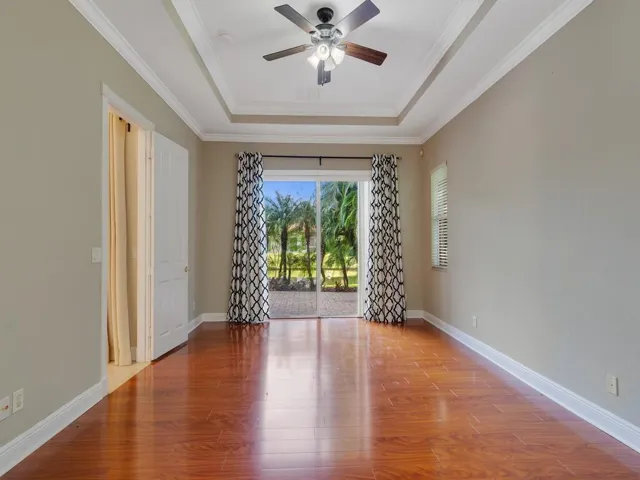 Bedroom with access to exterior, dark wood-style flooring, a tray ceiling, crown molding, and ceiling fan