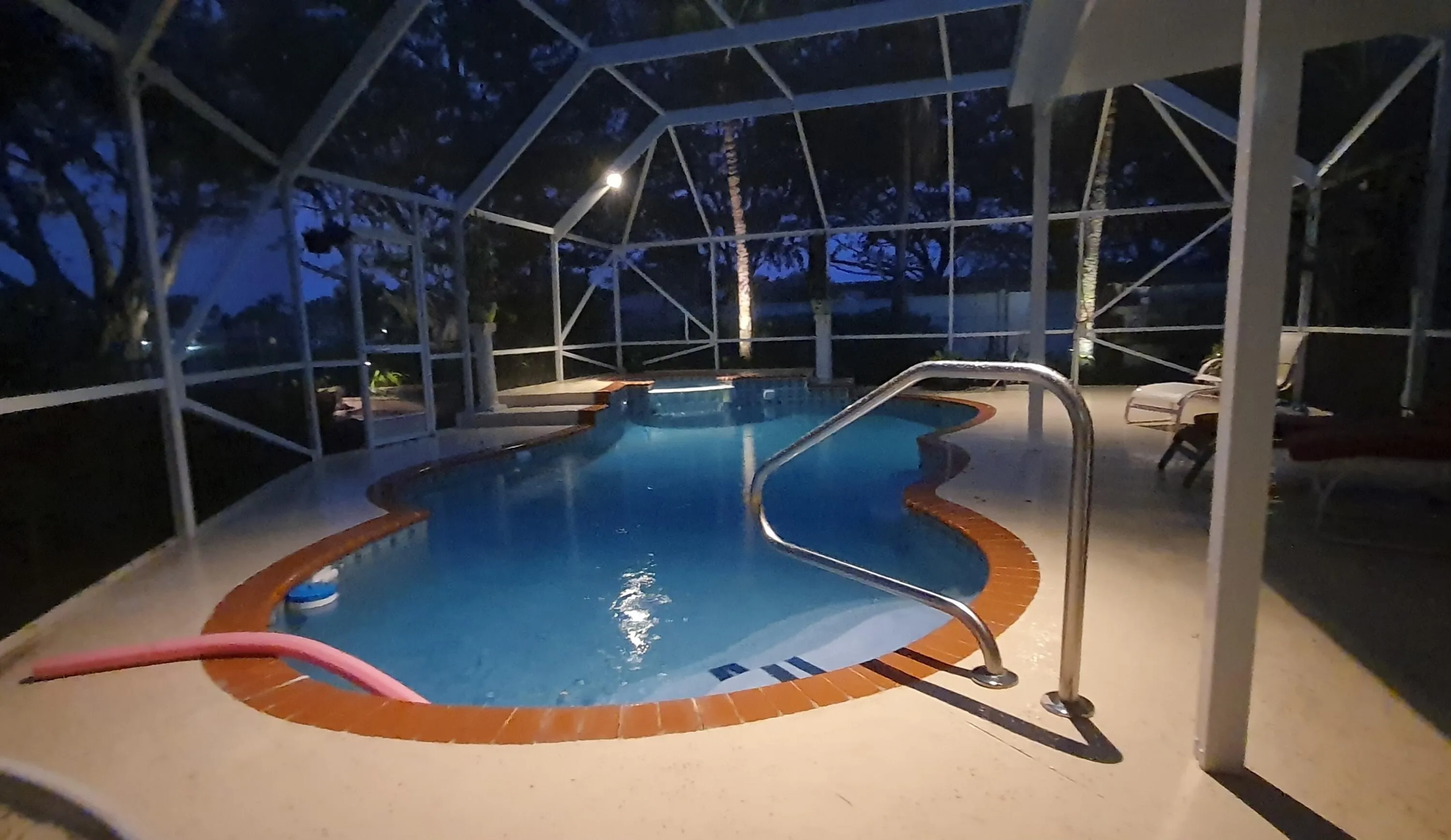 Screened pool enclosure featuring a freeform swimming pool with integrated spa, concrete deck, and perimeter lighting