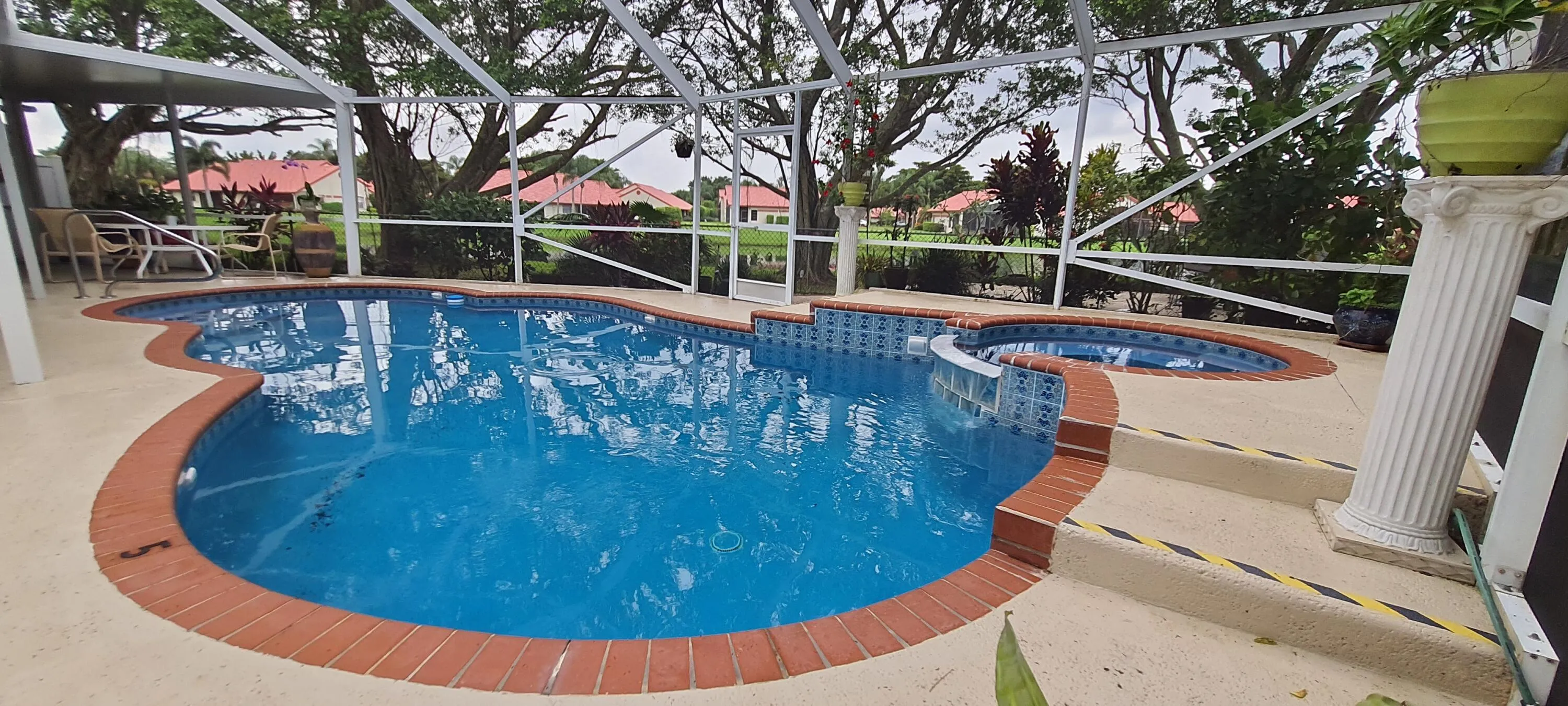 Screened-in pool deck featuring a freeform pool with brick coping, an integrated spa, and concrete pool deck
