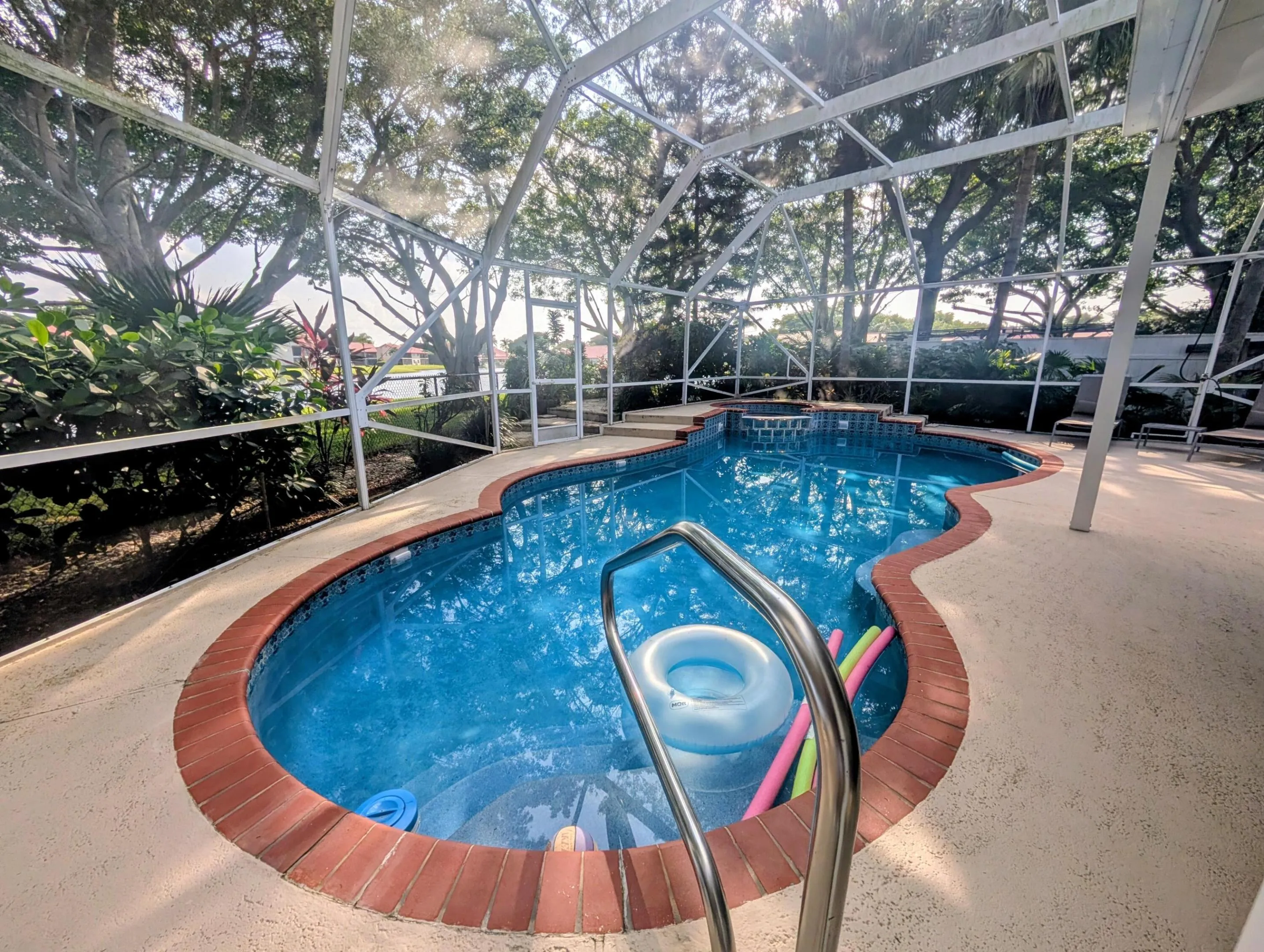Screened outdoor pool area featuring a freeform pool with a brick coping, a spa, and a light-colored concrete deck