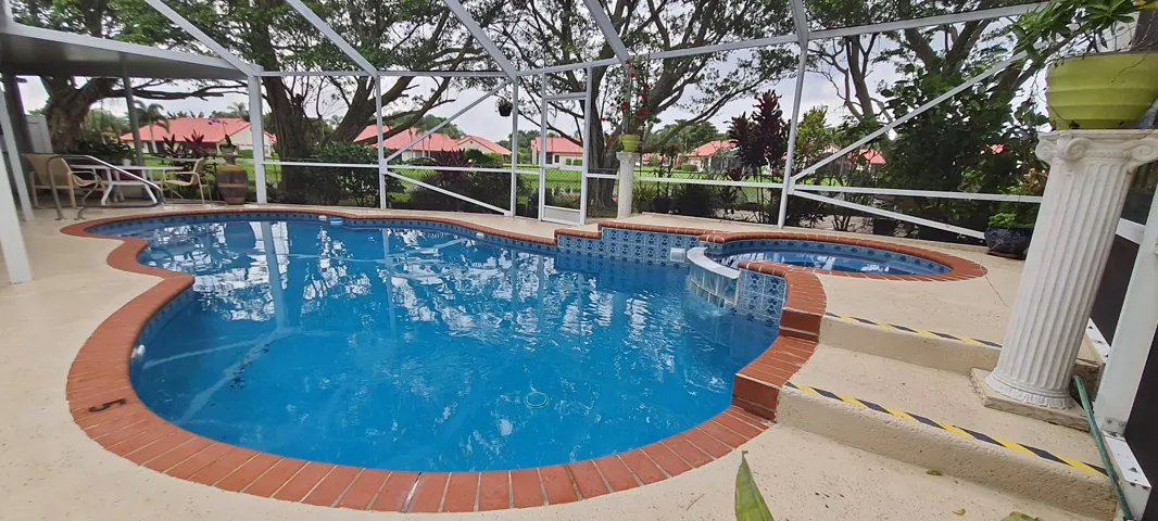 Screened-in pool deck featuring a freeform pool with brick coping, an integrated spa, and concrete pool deck