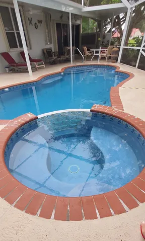 Screened lanai featuring a freeform swimming pool with integrated spa, blue tile interior, and brick coping