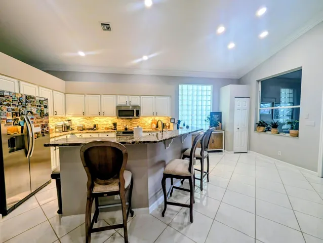 Spacious kitchen featuring white cabinetry, stone countertops, stainless steel appliances, and a tiled backsplash
