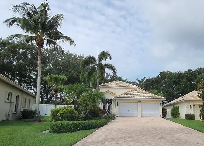 Tropical landscaping framing a residence with a light-colored exterior, two-car garage, and a paver driveway
