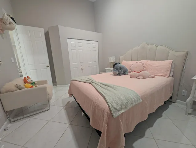 Bedroom featuring light grey wall paint, white tile flooring, a white paneled door, and bi-fold closet doors