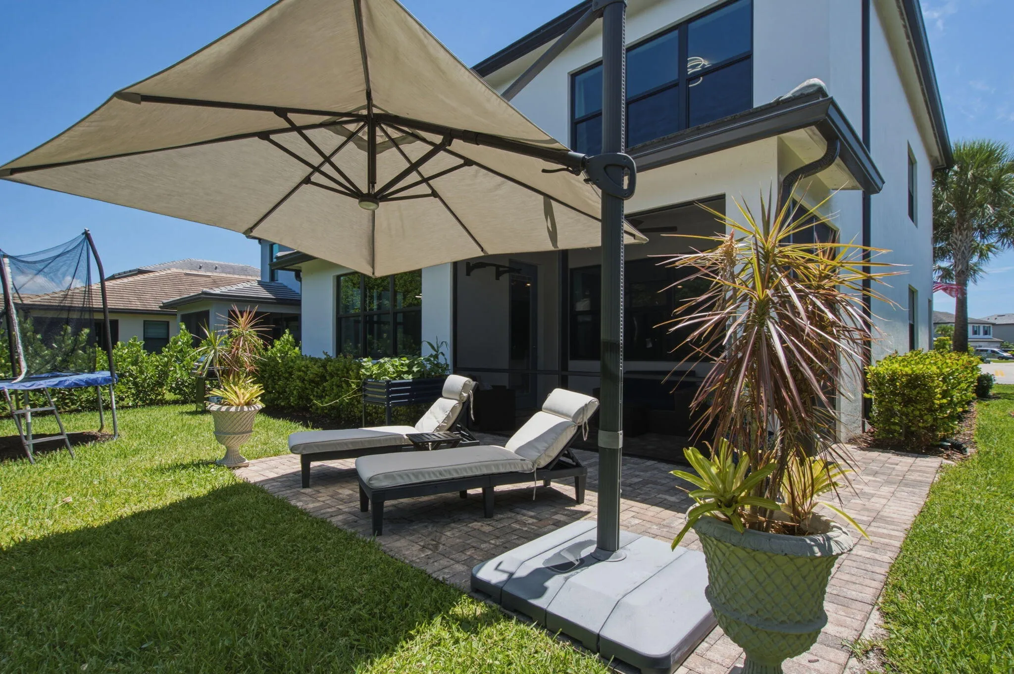 Expansive exterior patio featuring paver flooring, a large offset umbrella, and direct access to a manicured lawn