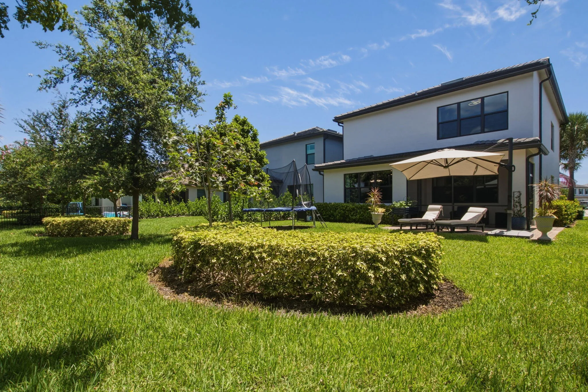 Rear exterior showcasing a white stucco facade with dark-framed windows, a covered patio, and a spacious green lawn