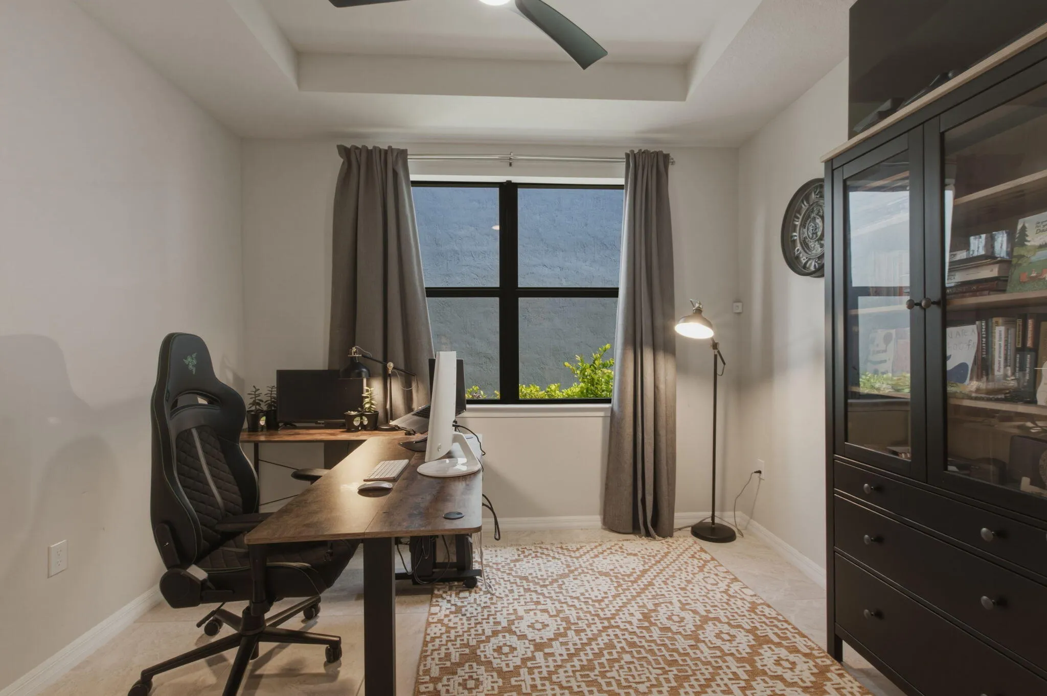 Interior room featuring a tray ceiling with a built-in ceiling fan, a large window with black framing, and neutral-toned walls