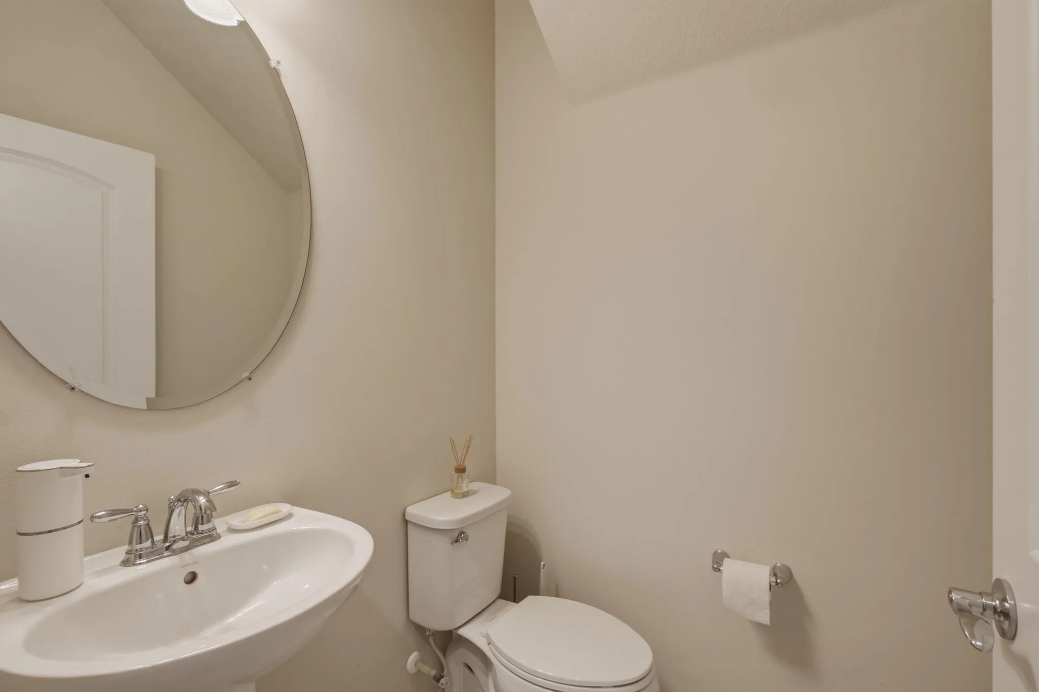 Pedestal sink with chrome faucet, complemented by a large circular mirror and overhead lighting