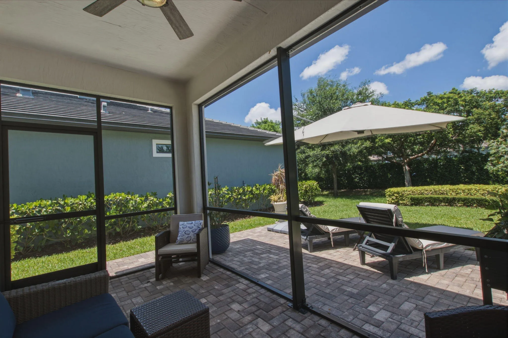 Screened patio featuring a ceiling fan, paver flooring, and a landscaped yard