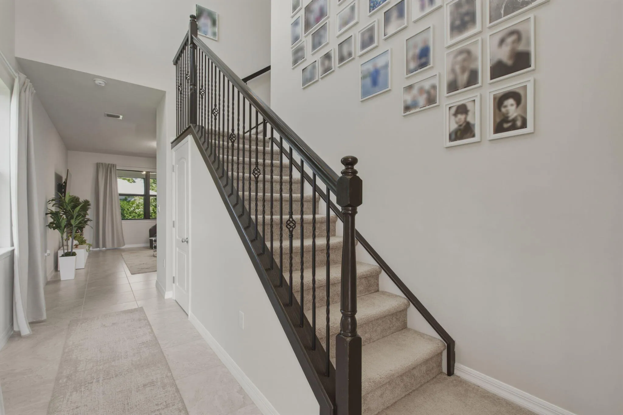 Staircase featuring dark iron balusters with decorative accents, carpeted treads, and a coordinating dark wood-finish newel post and handrail