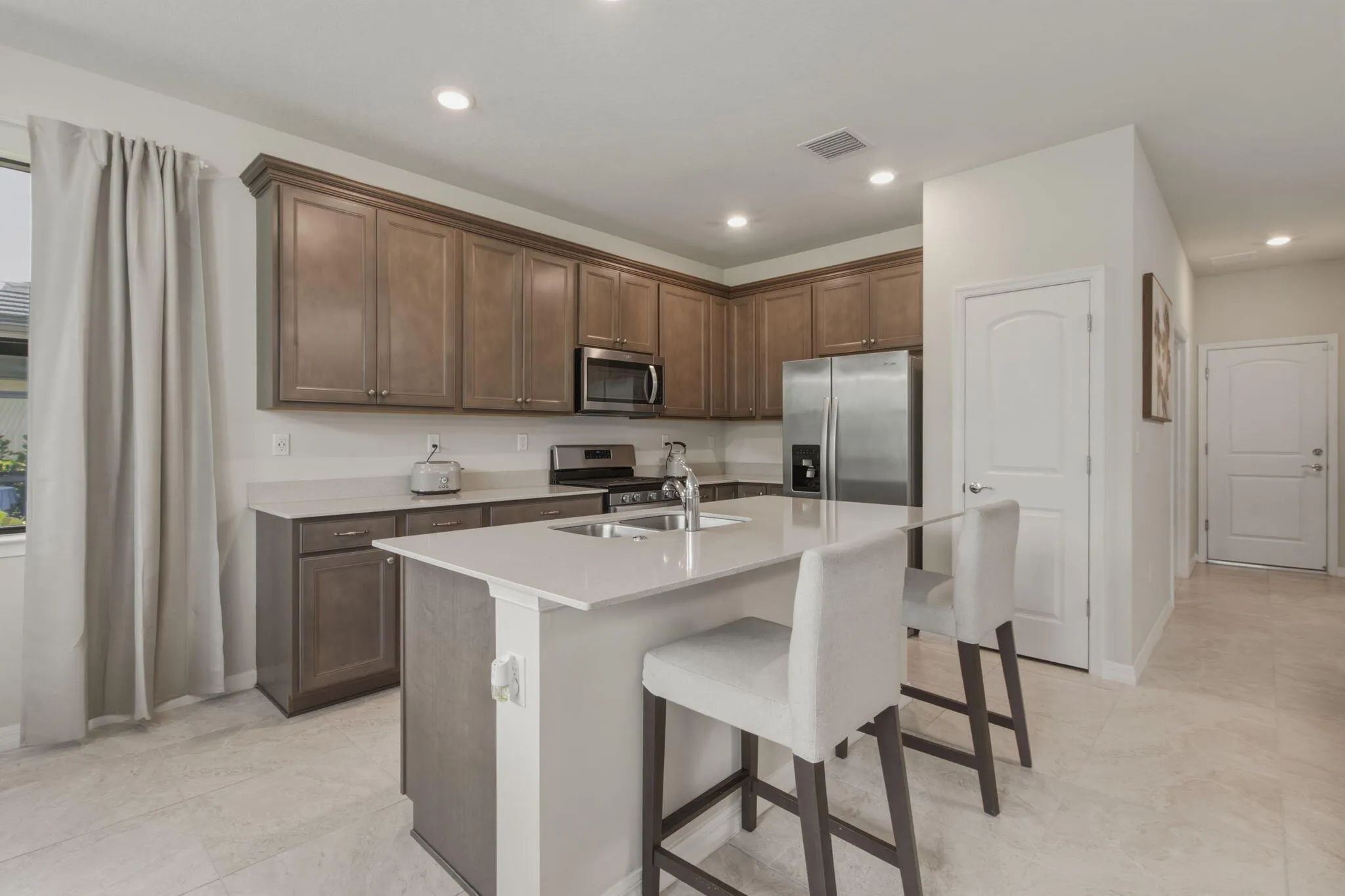 Modern kitchen featuring wood-finish cabinetry, stainless steel appliances, and an island with an undermount sink