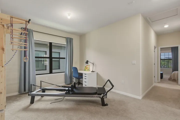 Spacious secondary room featuring neutral wall tones, plush carpeting, a large window with privacy blinds, and an overhead light fixture