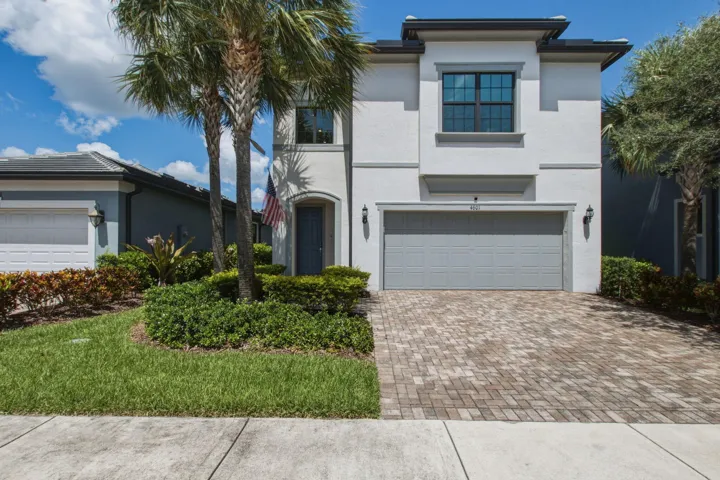 Contemporary stucco facade with a two-car garage, paver driveway, arched entry, and dark-framed windows