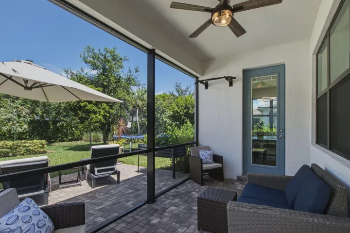 Screened patio featuring paver flooring, a ceiling fan, a glass-paneled door, and a private backyard with mature landscaping