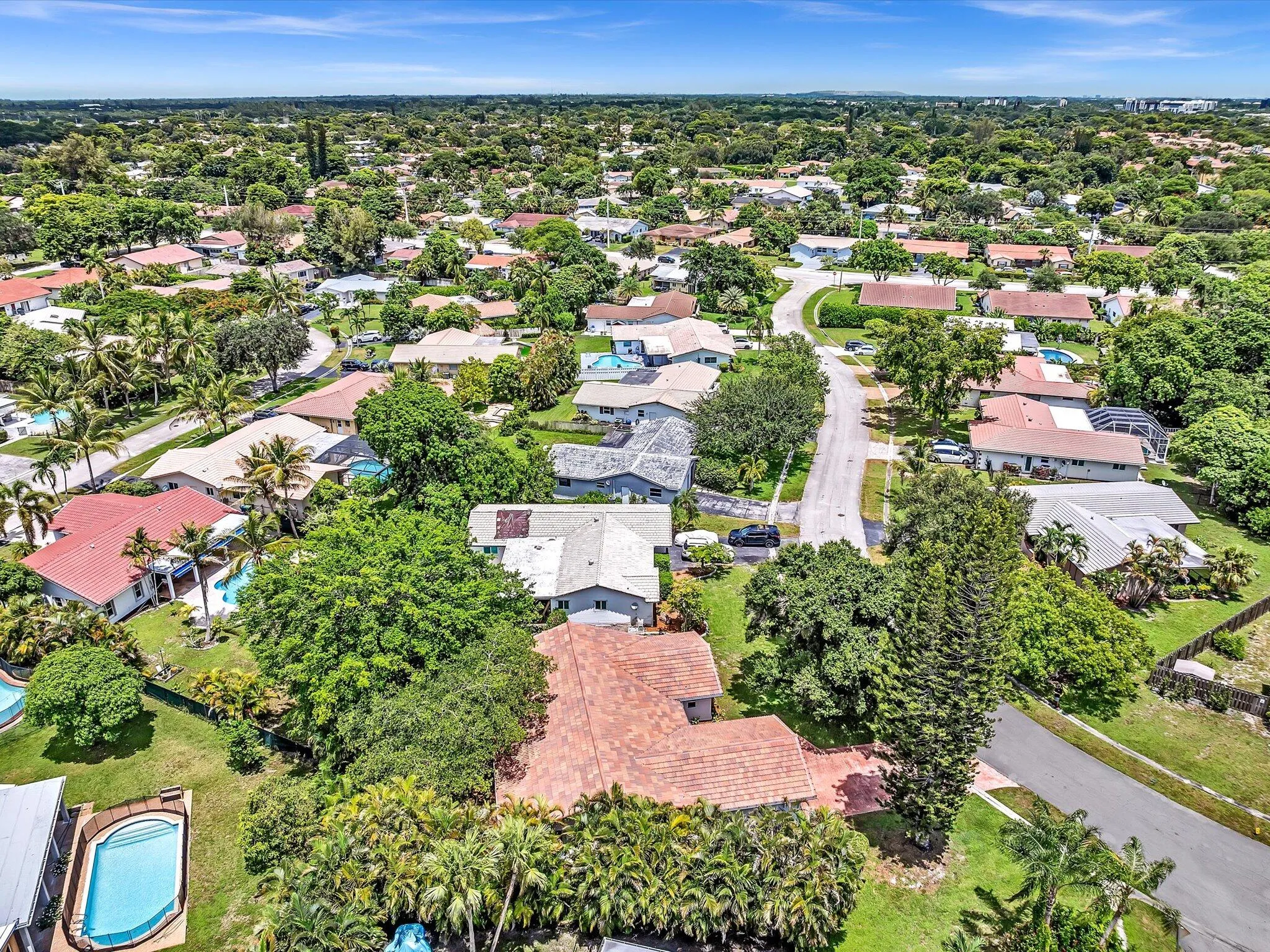 Aerial panorama showcasing a residential community with mature landscaping, numerous single-story properties, and private swimming pools