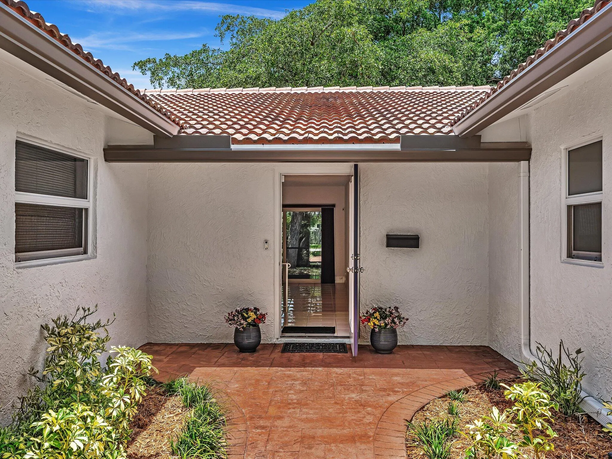 Covered entryway featuring a terracotta-tiled roof, textured stucco exterior, and a brick-patterned walkway