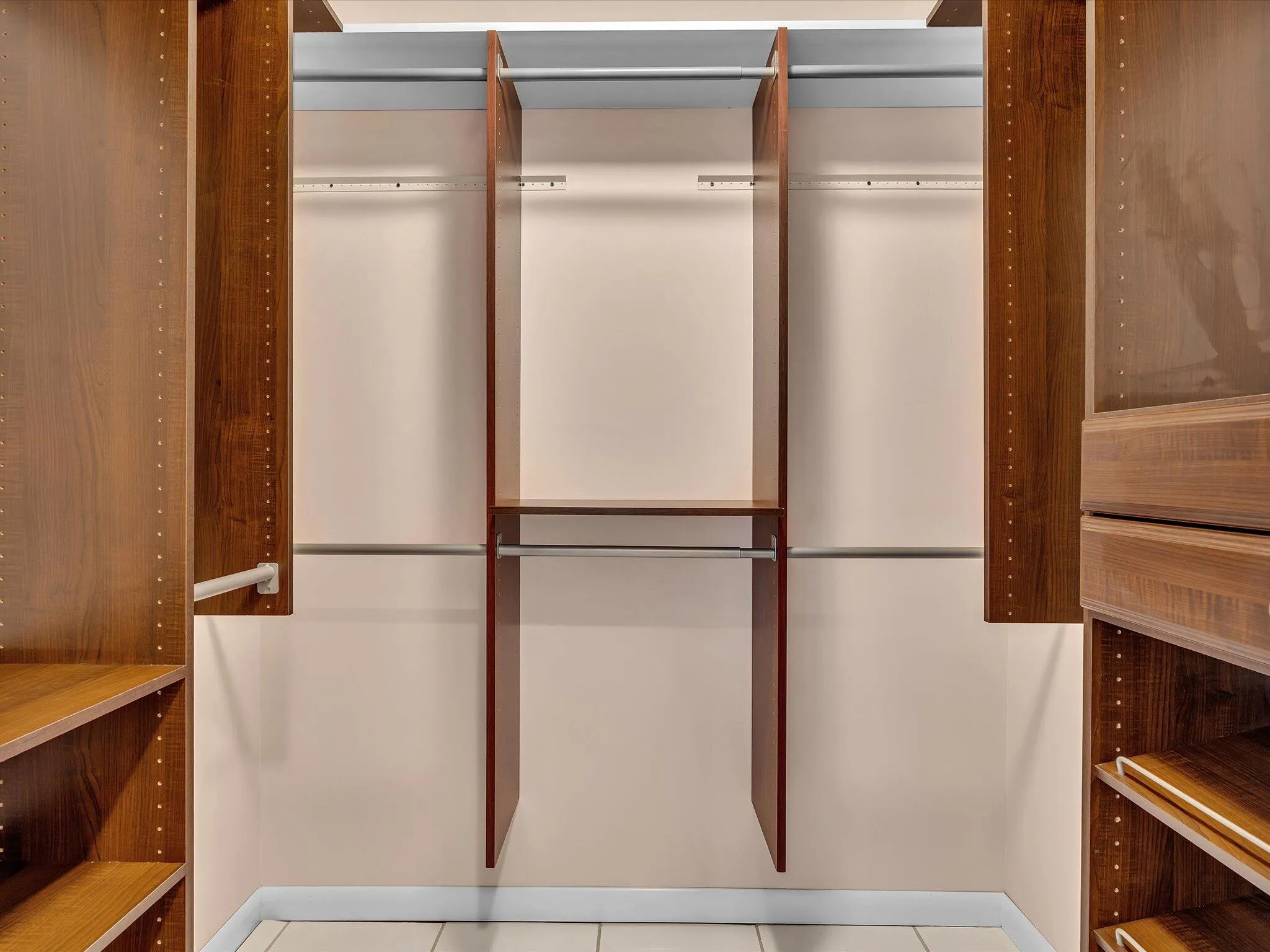 Walk-in closet featuring wood-finish shelving, multiple hanging rods, built-in drawer units, and tile flooring