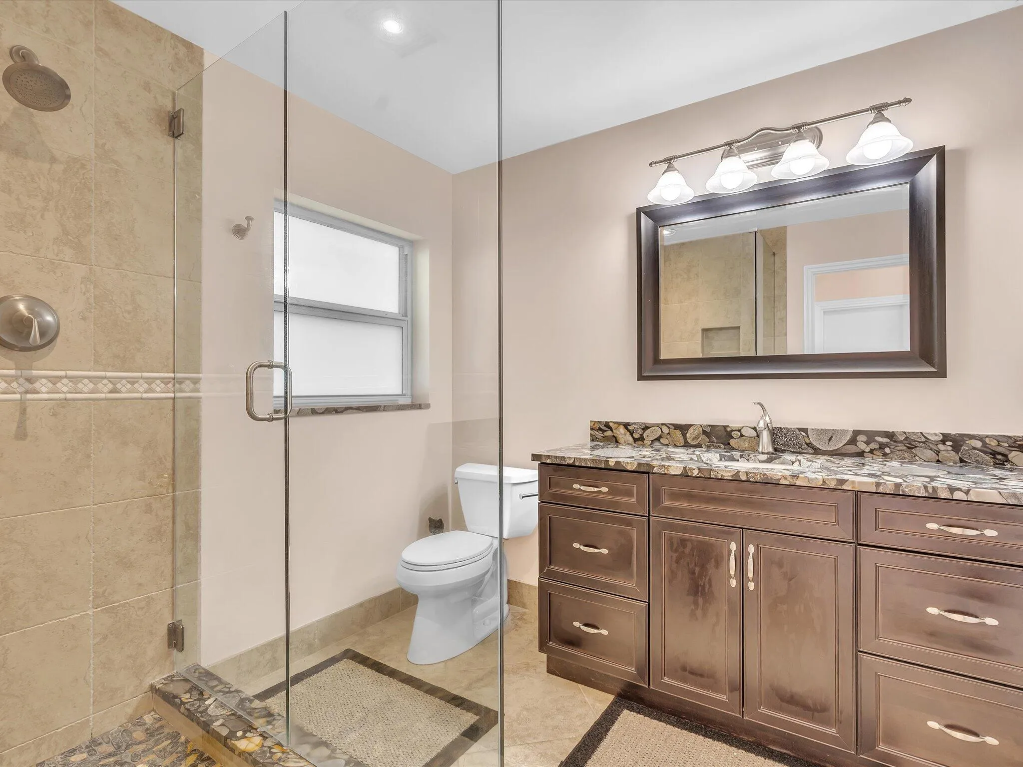 Bathroom featuring a glass-enclosed shower with tile surround, a dark wood-finish vanity with a stone countertop, an undermount sink, and a framed mirror with vanity lighting