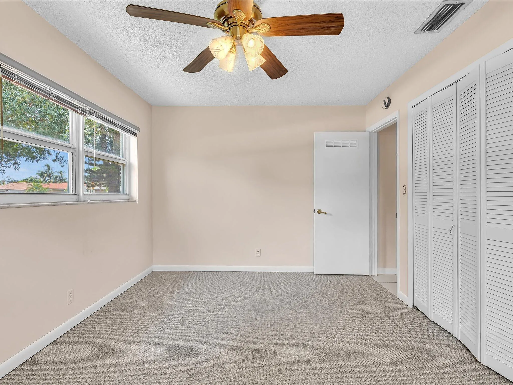 Neutral-toned room featuring a window with blinds, ceiling fan with light fixture, carpeted flooring, white bifold closet doors, and white interior doors