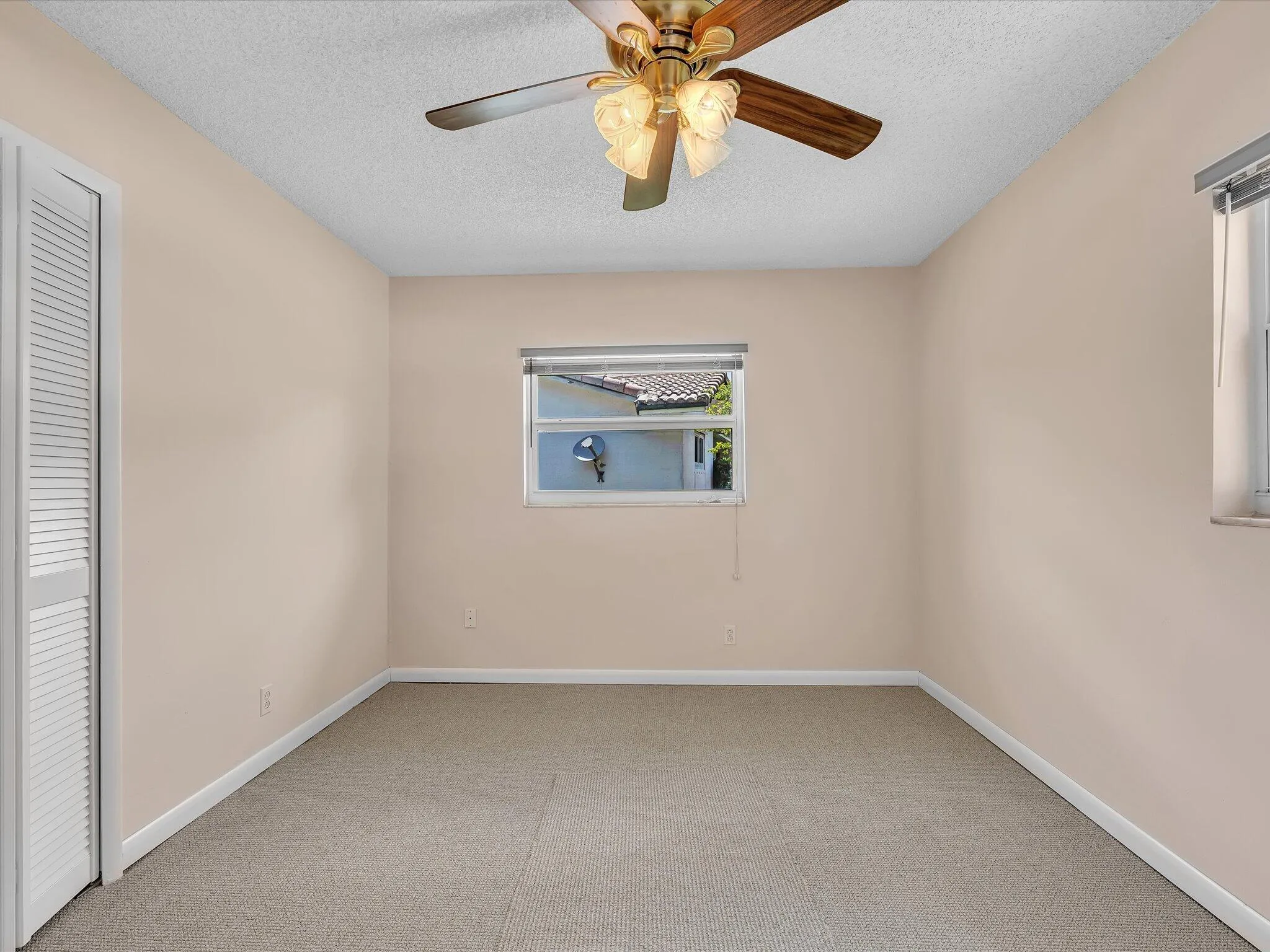 Carpeted room featuring a ceiling fan with integrated lighting, a window with horizontal blinds, and a louvered bi-fold closet door