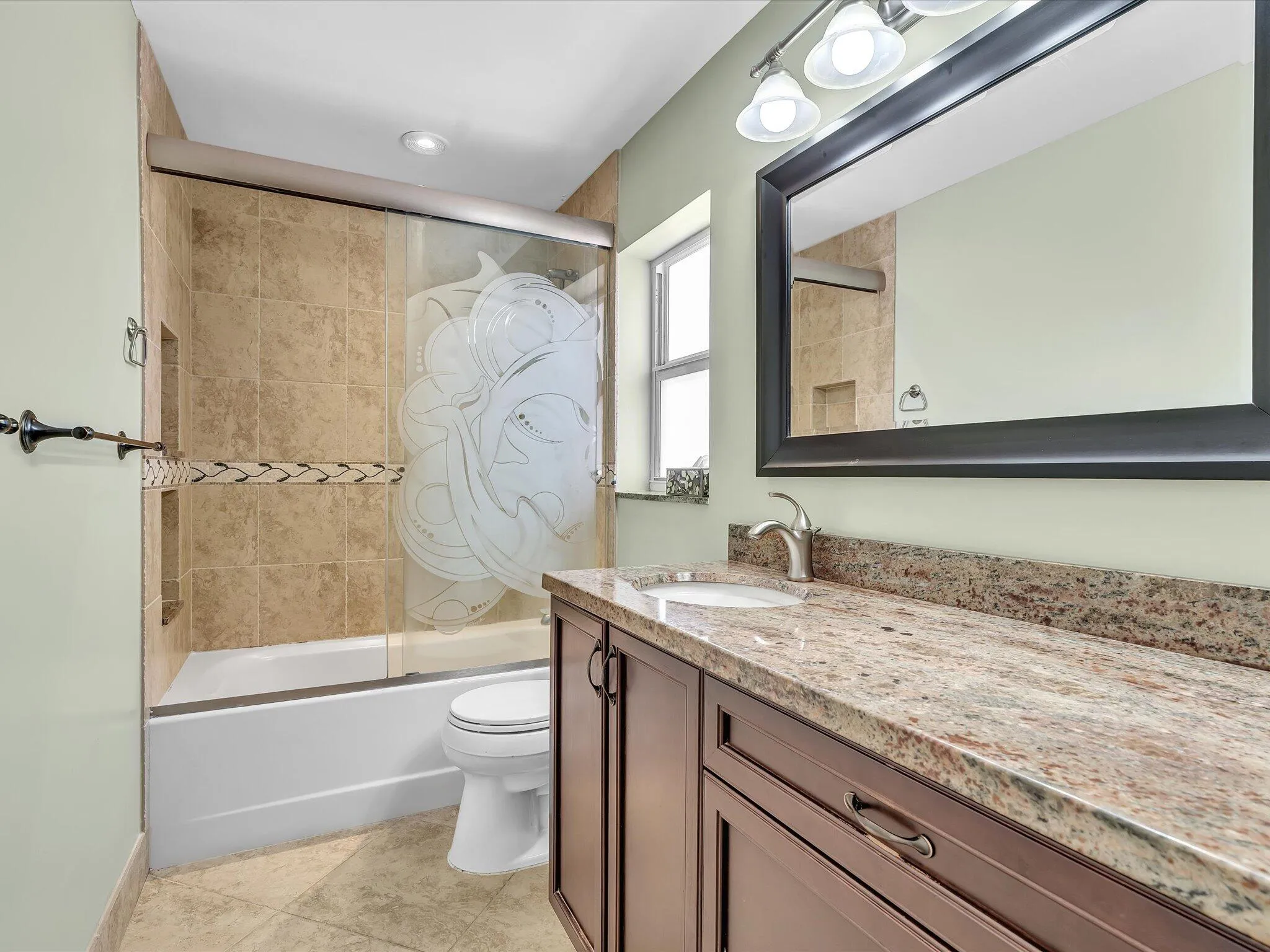 Bathroom featuring a brown wood-finish vanity with a stone countertop, an undermount sink, and a framed mirror