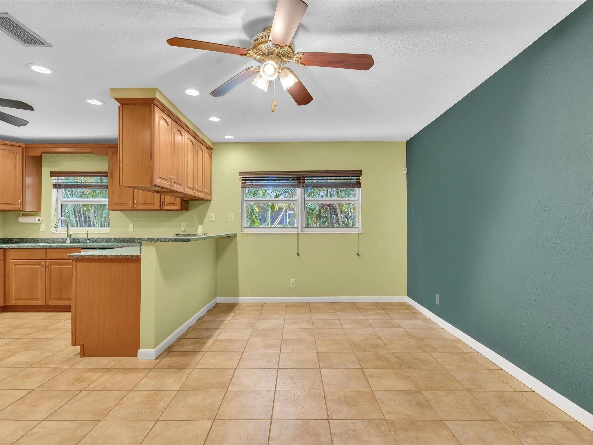 Open-concept area featuring light tile flooring, a kitchen with wood cabinetry and light countertops, and a ceiling fan with integrated lighting