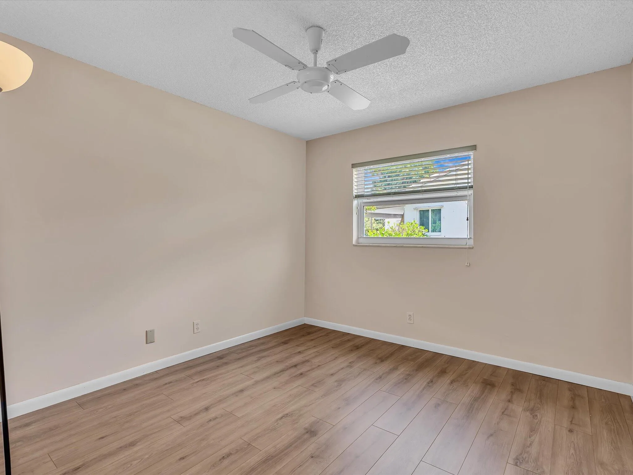 Interior room featuring wood-finish flooring, a ceiling fan with light fixture, a window with horizontal blinds, and neutral wall paint