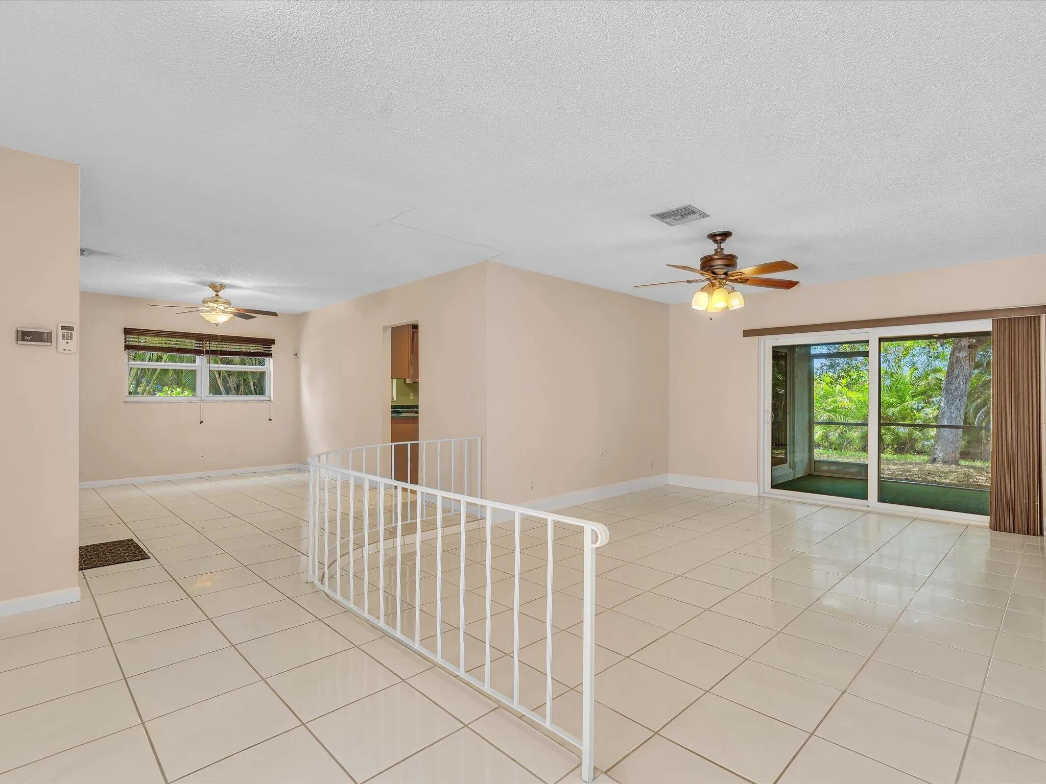Open-concept living area with large format tile flooring, a patio door to exterior, and multiple ceiling fans