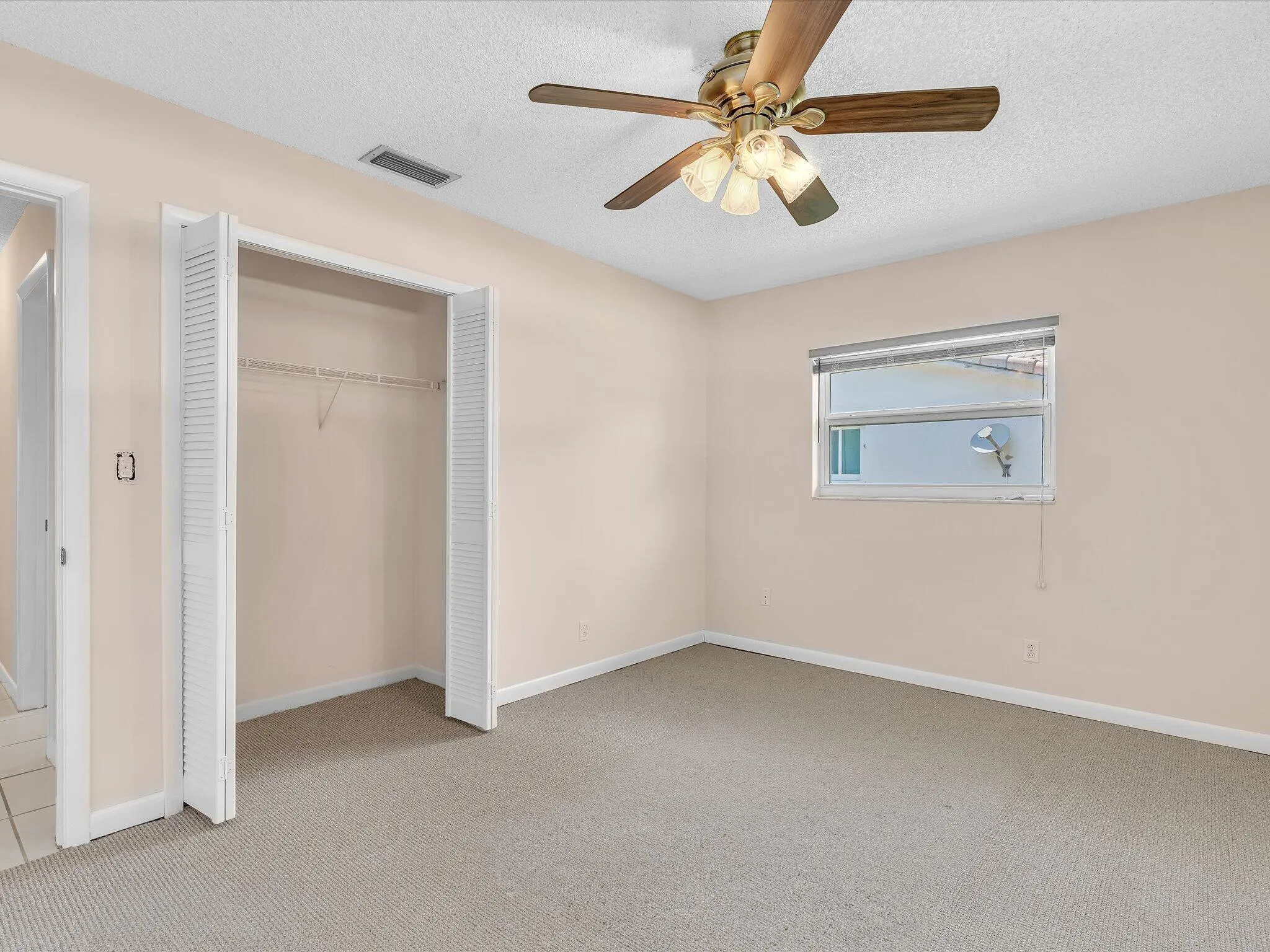 Carpeted room featuring a ceiling fan with integrated lighting, a window with horizontal blinds, and a bi-fold louvered closet