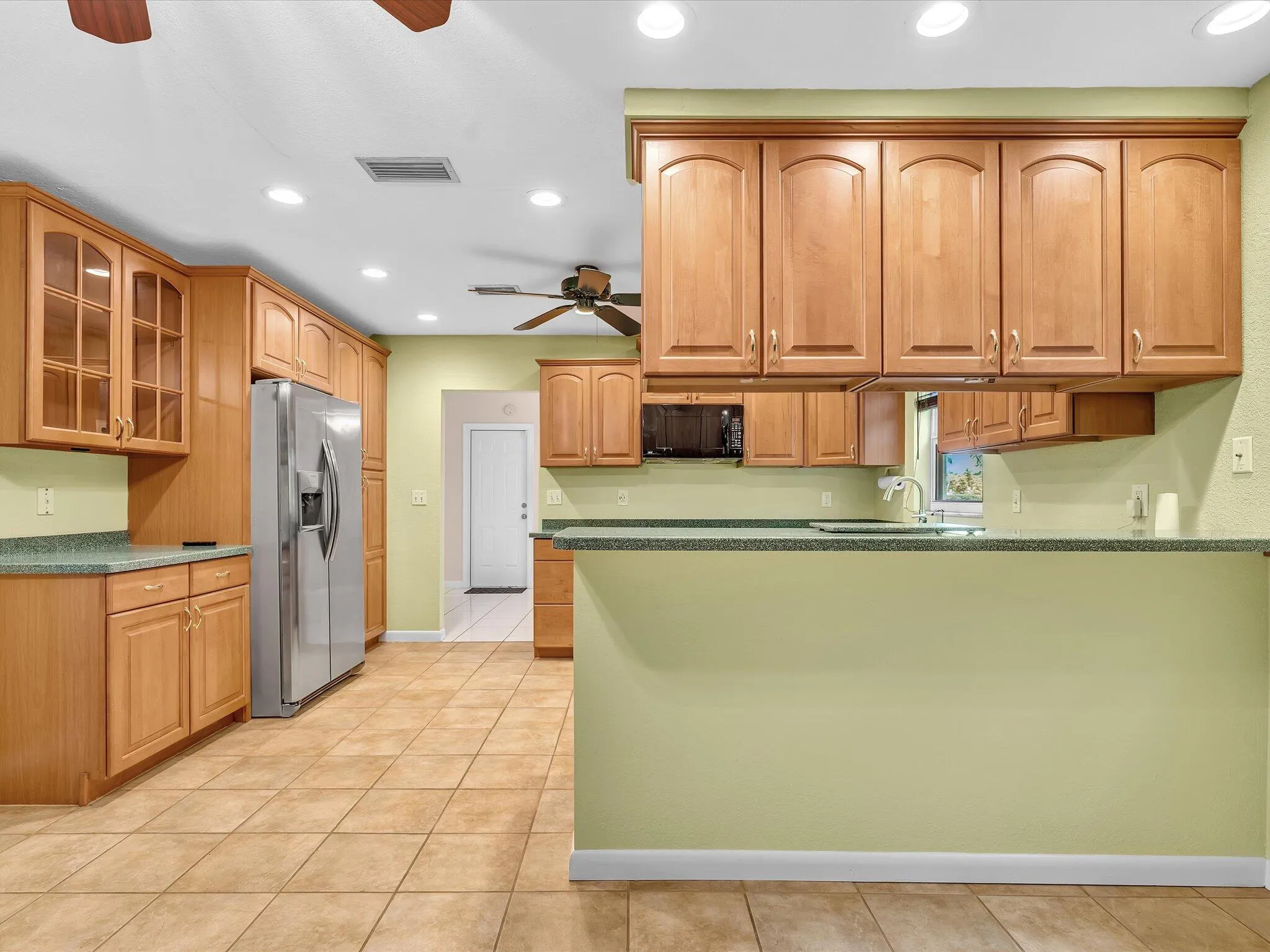 Spacious kitchen featuring extensive wood cabinetry, tile flooring, recessed ceiling lighting, and a kitchen island with a built-in sink