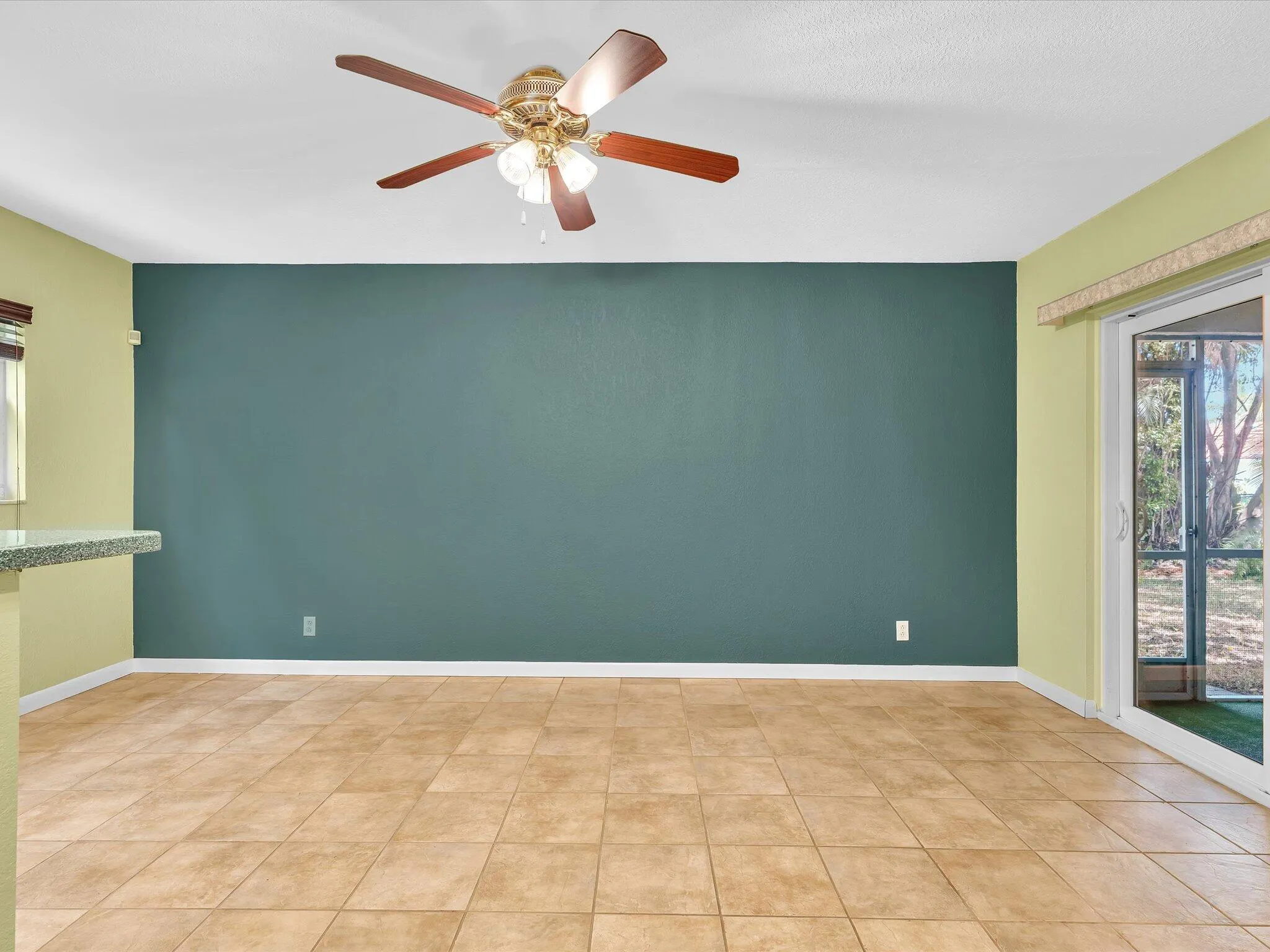 Open-concept room featuring warm-toned tile flooring, a built-in ceiling fan with light fixture, and a sliding glass door providing access to the outdoors