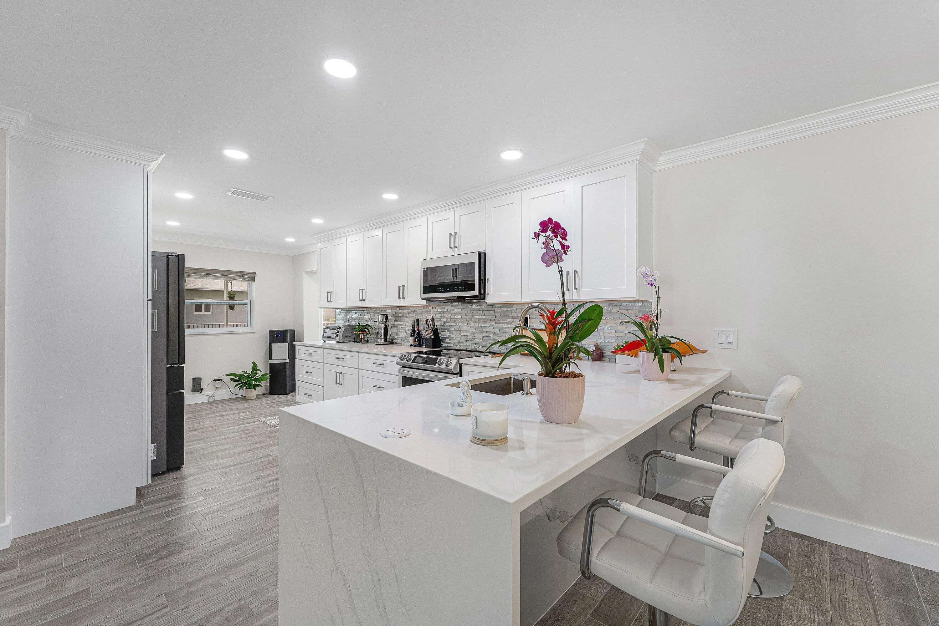 Kitchen featuring a large waterfall island with a light-toned countertop, white shaker cabinetry, stainless steel appliances, and wood-finish flooring