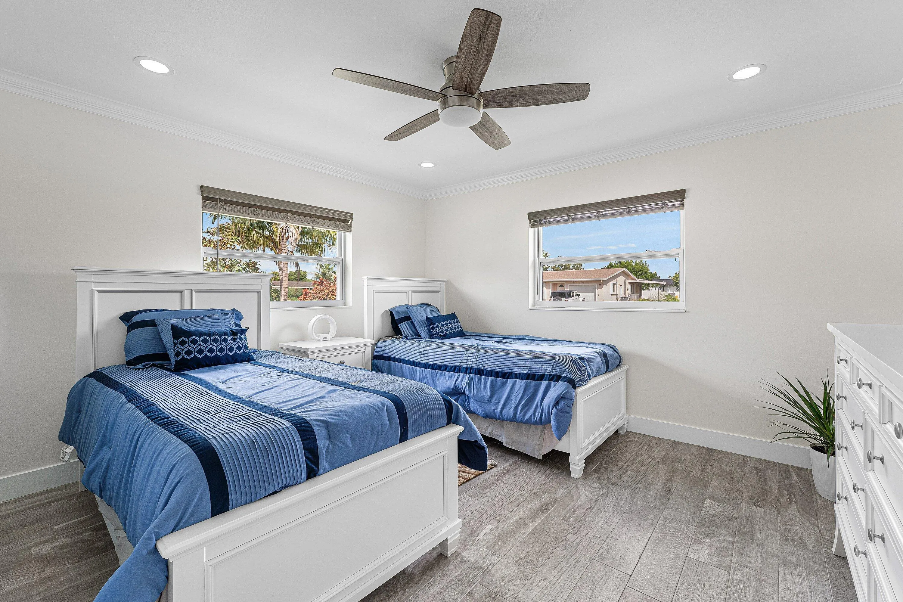 Bright room featuring two windows with roller shades, a ceiling fan with light fixture, recessed lighting, and wood-finish flooring