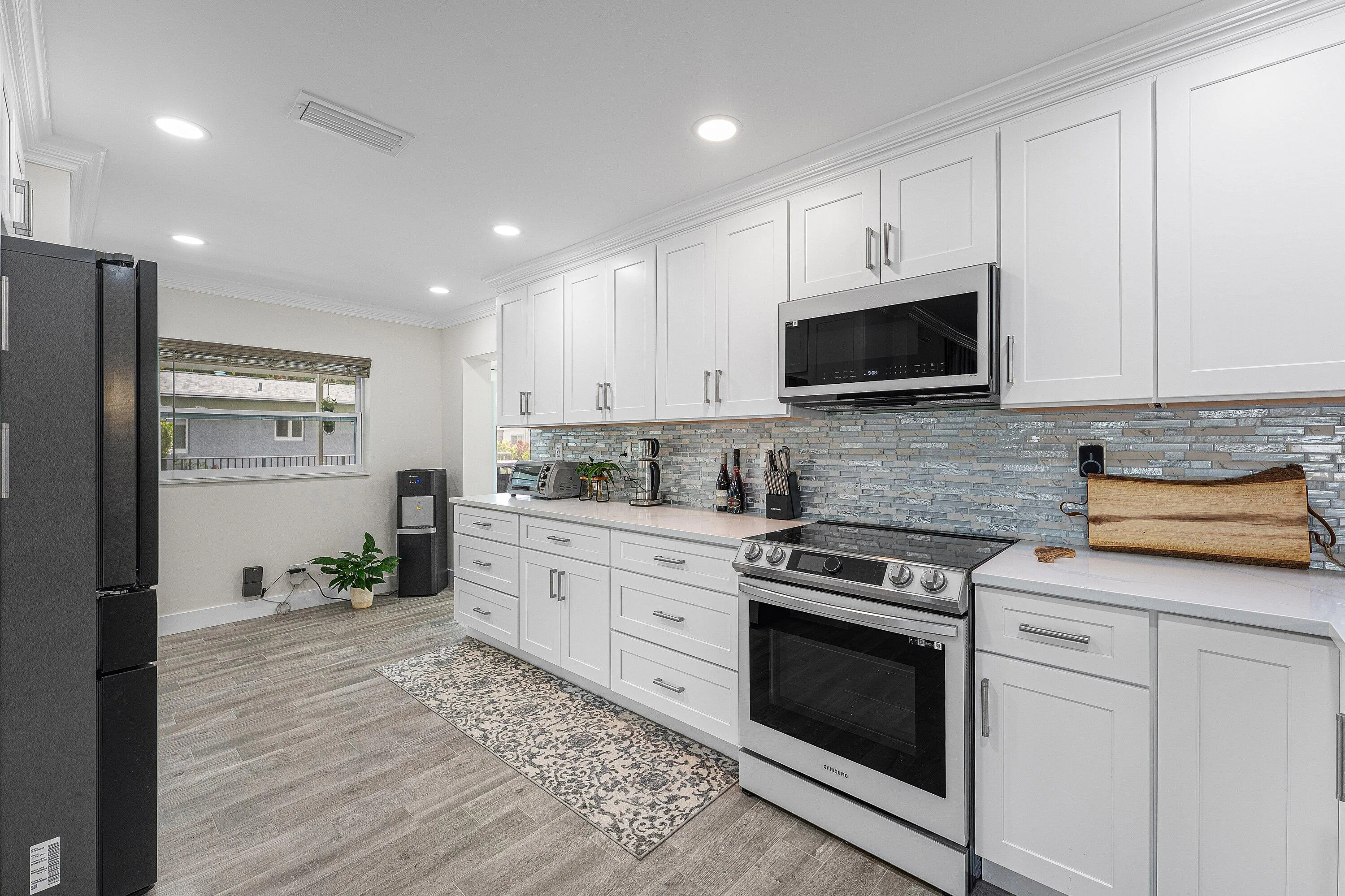 Modern kitchen featuring extensive white shaker cabinetry, stainless steel appliances, a linear tile backsplash, and light-toned countertops