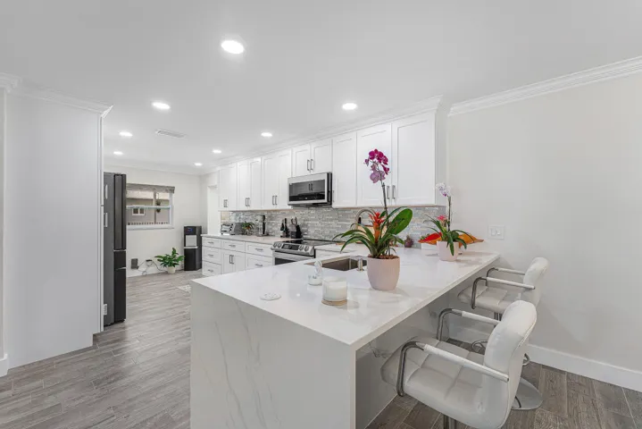 Kitchen featuring a large waterfall island with a light-toned countertop, white shaker cabinetry, stainless steel appliances, and wood-finish flooring