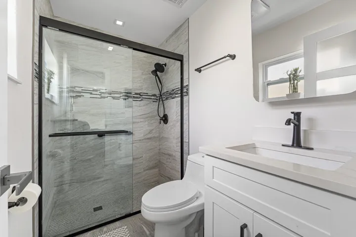 Sleek bathroom featuring a frameless glass shower enclosure with matte black hardware, a tiled shower interior with mosaic accent band, a white vanity with integrated sink and quartz countertop, and a contemporary matte black faucet