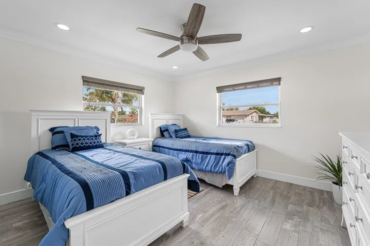 Bright room featuring two windows with roller shades, a ceiling fan with light fixture, recessed lighting, and wood-finish flooring