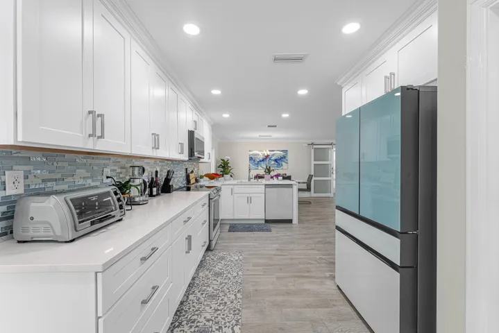 Modern kitchen featuring extensive white cabinetry with crown molding, light-toned countertops, and a blue and white mosaic tile backsplash