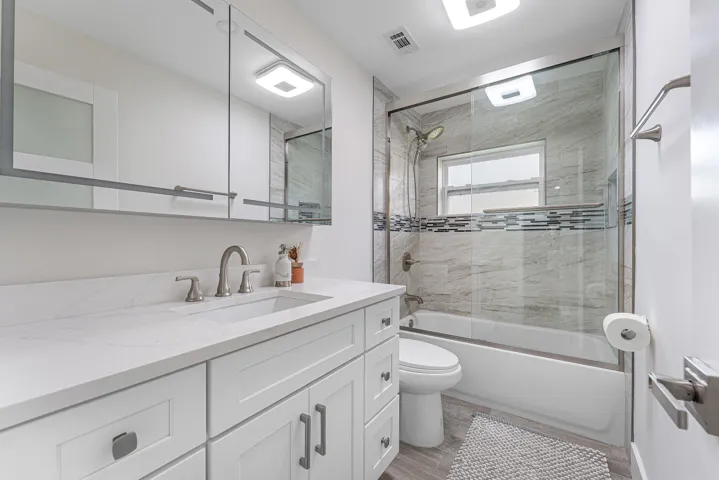 Contemporary bathroom featuring a white vanity with an integrated sink and brushed nickel faucet, complemented by a large mirrored medicine cabinet