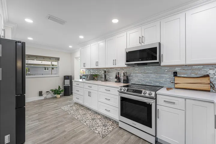 Modern kitchen featuring extensive white shaker cabinetry, stainless steel appliances, a linear tile backsplash, and light-toned countertops
