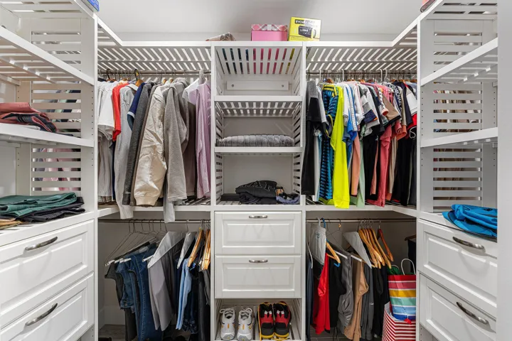 Custom closet system featuring white cabinetry with shaker-style drawer fronts, chrome hardware, open shelving, and hanging rods