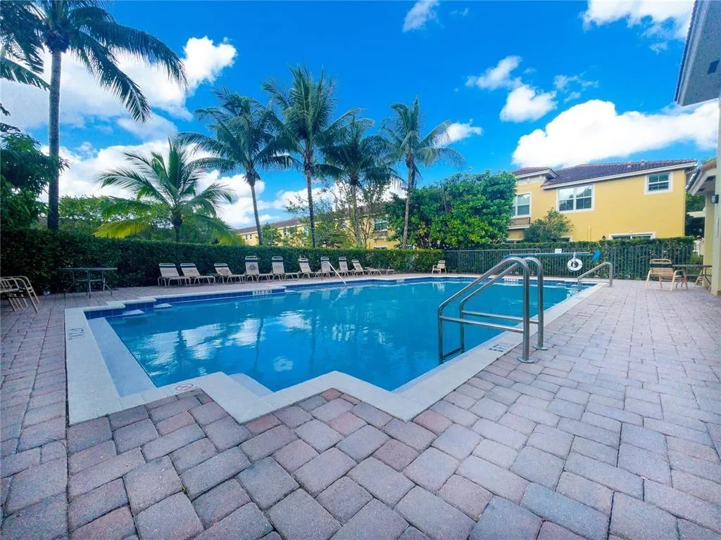 Outdoor swimming pool with integrated steps, surrounded by paver patio surfacing, lush perimeter hedging, and mature palm trees