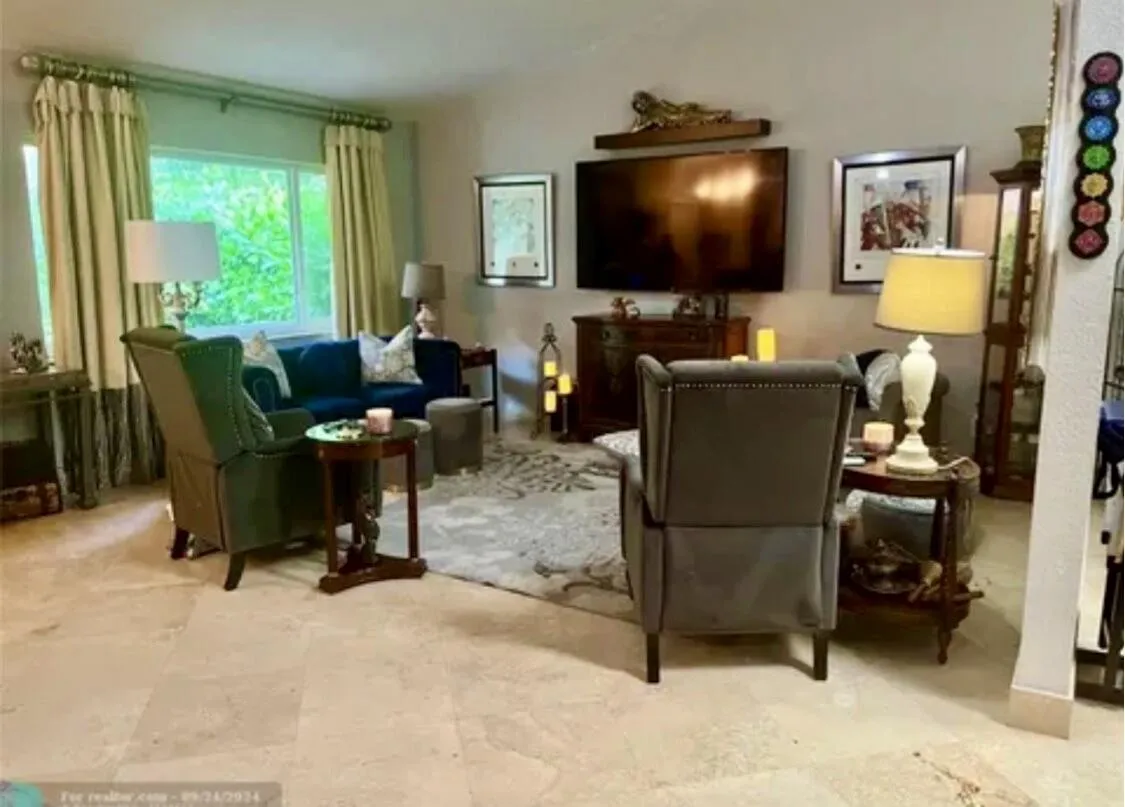 Spacious living area featuring light-toned tile flooring, vaulted ceilings, and a large window