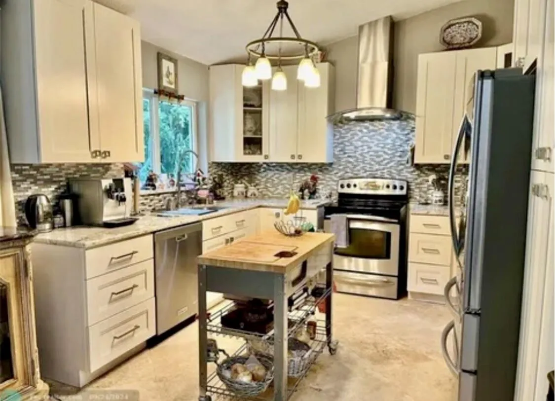 Well-appointed kitchen featuring light-toned cabinetry, stainless steel appliances, a mosaic tile backsplash, and a central island with a wood countertop