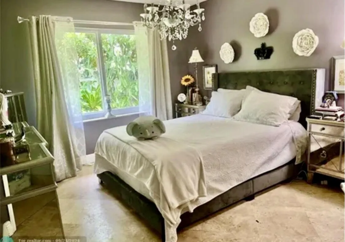 Bedroom featuring a tufted upholstered headboard, a large window with sheer and blackout drapes, and a decorative crystal chandelier