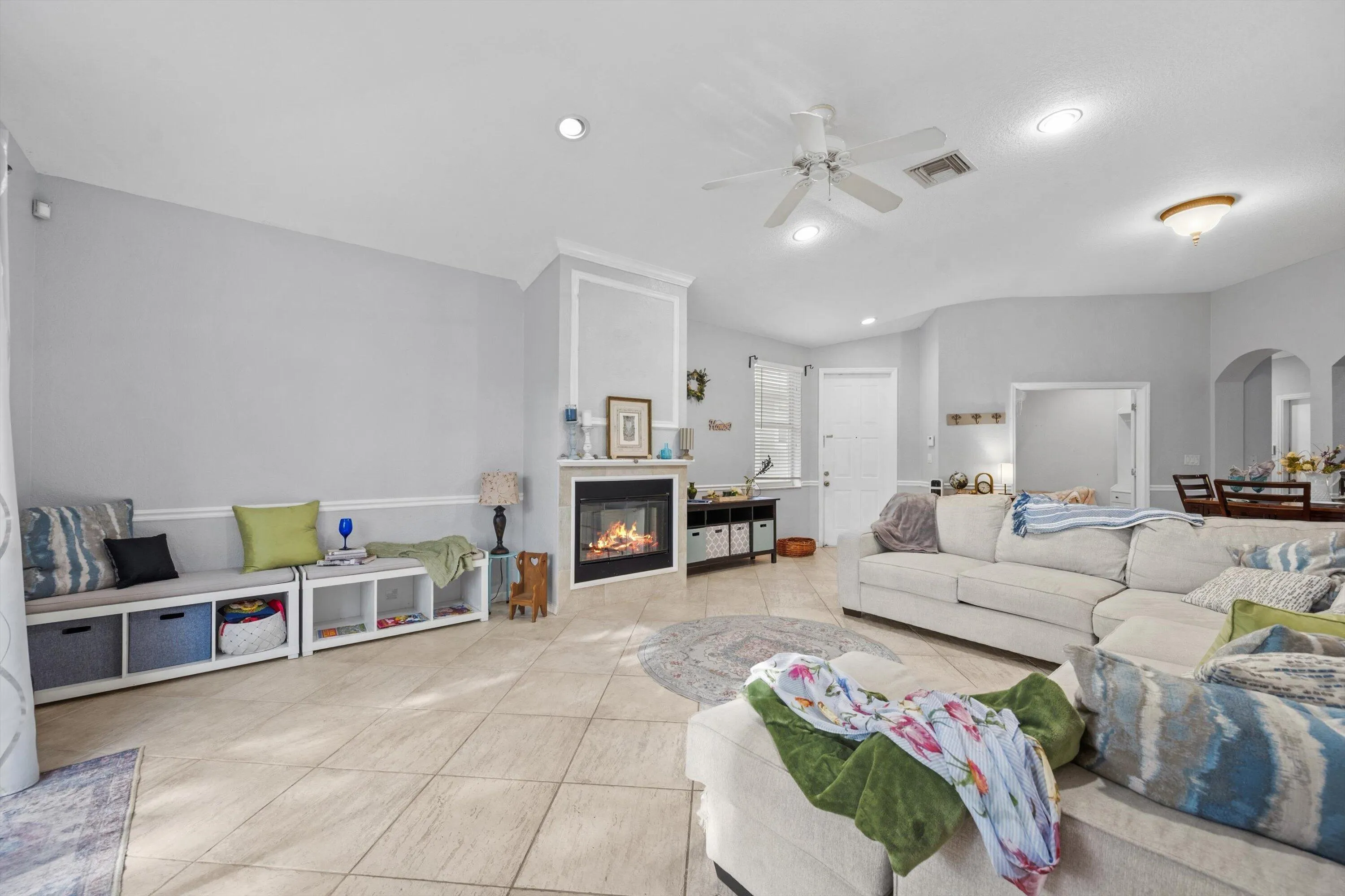 Expansive living area featuring light-toned tile flooring and a corner fireplace with white trim