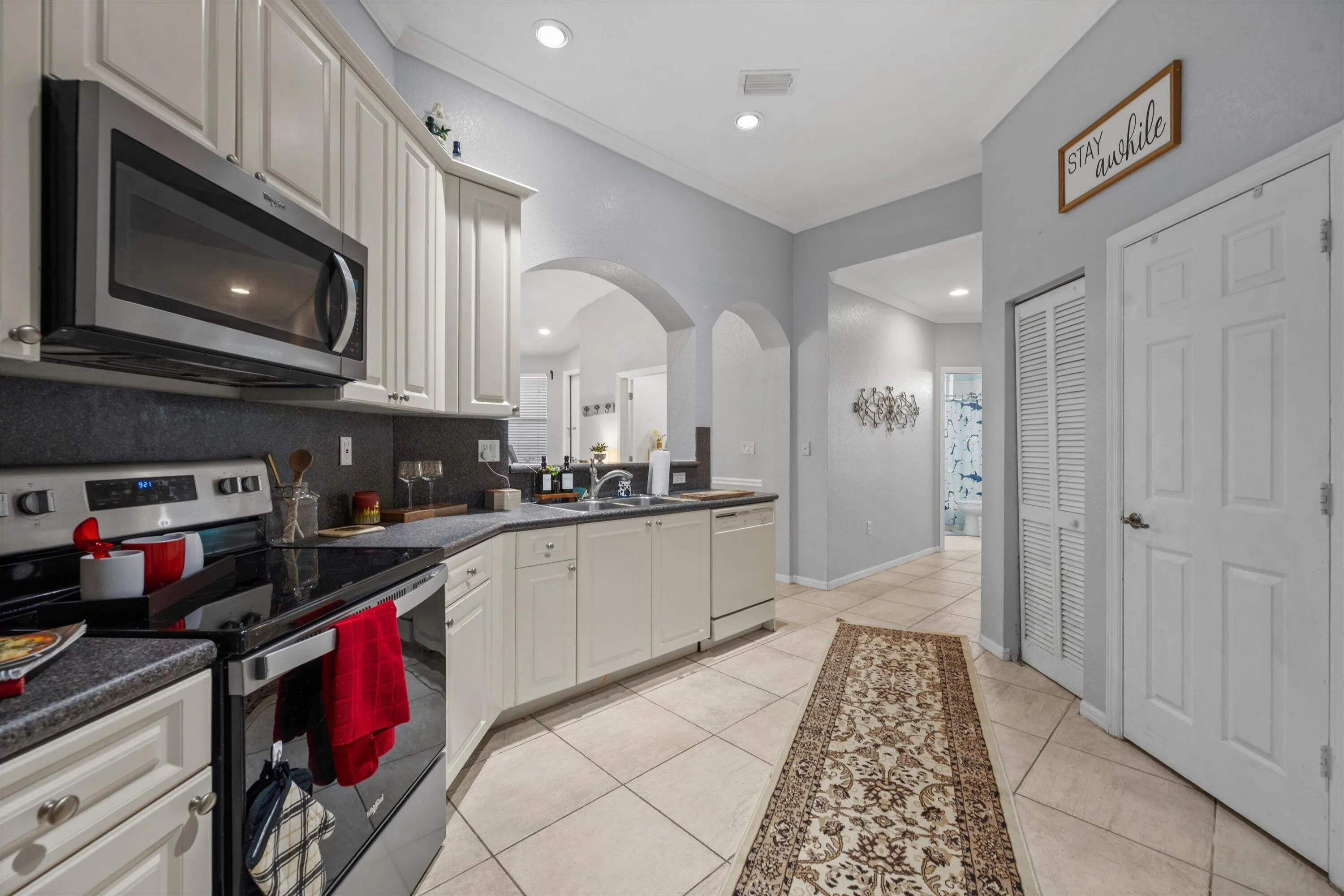 Kitchen featuring white cabinetry, stainless steel appliances, dark countertops, and a tile backsplash