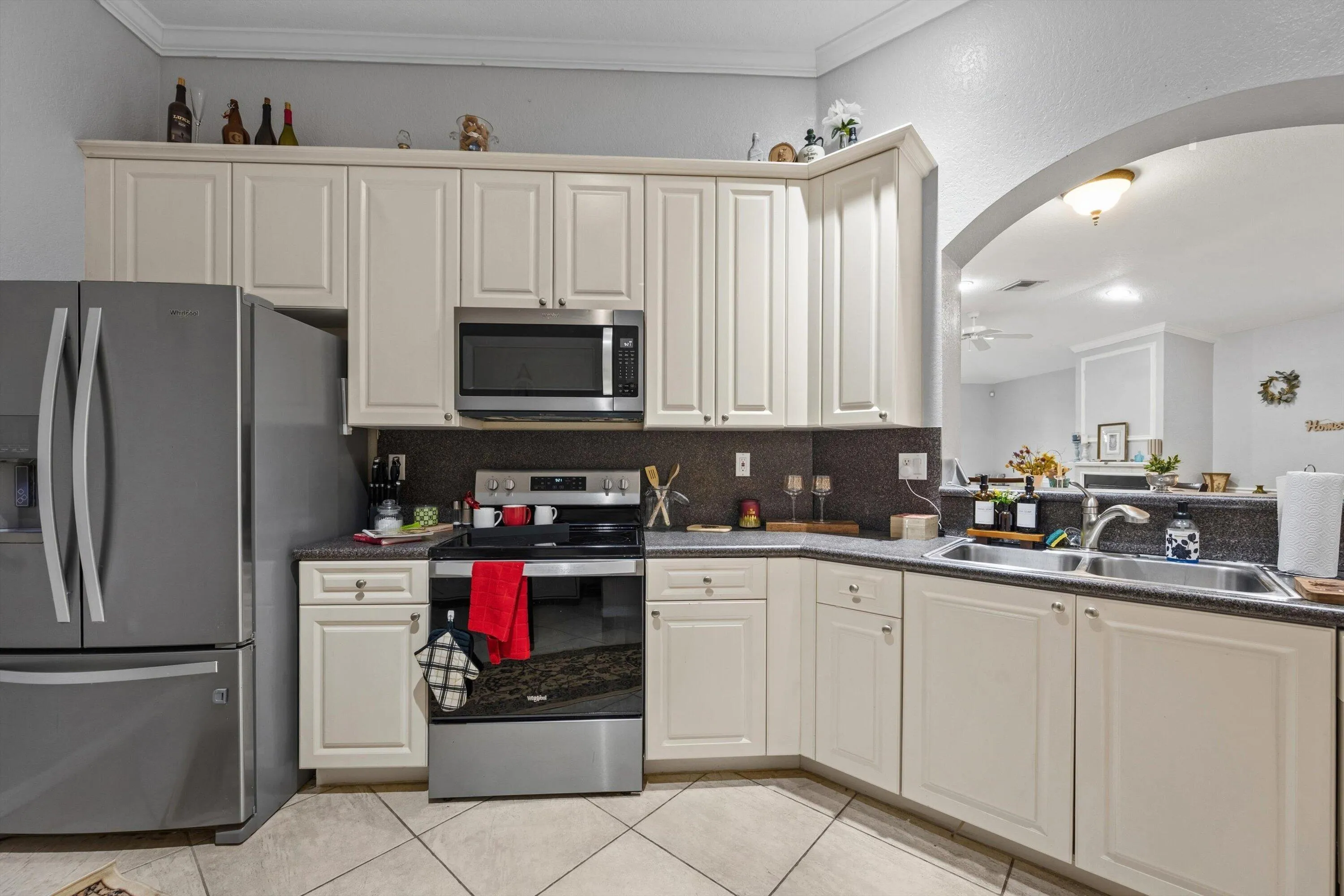 Kitchen featuring off-white cabinetry, dark countertops, a stainless steel side-by-side refrigerator, stainless steel range, and an integrated double basin sink
